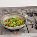 A Vollrath Wear-Ever aluminum non-stick fry pan with vegetables cooking in it on a stove.