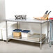 An Advance Tabco stainless steel work table with a metal shelf holding containers of food.