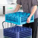 A blue Carlisle OptiClean 16 compartment glass rack with 2 extenders being handled in a commercial kitchen setting.