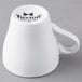 A white porcelain espresso cup with a handle and the word "Tuxton" on it.