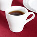 Two white Tuxton espresso cups filled with brown liquid on a table.