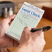 A green and white guest check pad with beverage lines and a top guest receipt being written on by a person.