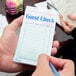 A hand holding a green and white Choice guest check with a pen.