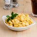 A Tuxton eggshell white round bowl filled with macaroni and cheese on a table.