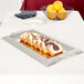 A Vollrath rectangular stainless steel serving tray with slices of cake on a table.