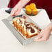 A person holding a Vollrath rectangular stainless steel serving tray with handles full of sliced bread.
