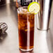 A Libbey Straight Sided glass of iced tea with a lime slice on top.