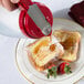 A person using a Tablecraft red polyethylene dispenser to pour syrup on a plate of french toast.