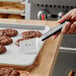 A hand holding a Mercer Culinary Mini Turner with a black handle over a tray of chocolate cookies.