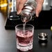 A person using a Vollrath stainless steel cobbler cocktail shaker to pour a pink drink into a glass.