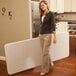 A woman holding a Lifetime almond plastic rectangular folding table.