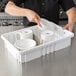 A person holding a white dishware in a white Metro tote box with dividers.