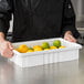 A person holding a Metro white divider tote box filled with lemons and limes.