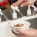 A person using a Carlisle pump condiment dispenser to pour brown liquid into a bowl of ice cream.