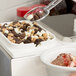 A person using a Carlisle pump to dispense chocolate and nuts onto a bowl of ice cream.