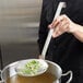 A person using a Vollrath round skimmer to stir a pot of food.