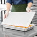 A person holding a Vollrath stainless steel steam table pan lid over a tray of food.