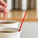 A red and white coffee stirrer placed in a paper cup filled with a hot beverage.