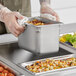 A person holding a Vollrath stainless steel steam table pan full of food.