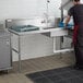 A man washing dishes on a Regency soiled dish table in a professional kitchen.