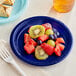 A navy blue plastic plate with fruit on it next to a fork.