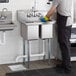 A man wearing gloves washing dishes in a Regency two compartment sink.