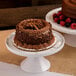 An Elite Global Solutions faux Carrara marble round plate stand holding two chocolate cakes with berries on top.