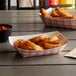 A group of fried food in red check paper food trays with red sauce on a table.