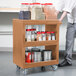 A man pushing a Cambro beige plastic service cart full of food items.