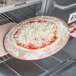 A person using an American Metalcraft round pizza peel to put a pizza in the oven.