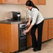 A woman using a Follett undercounter ice and water dispenser to fill a cup with water.