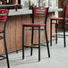 A Lancaster Table & Seating bar stool with mahogany wood seat and back at a bar counter.