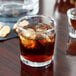 An Anchor Hocking Regency old fashioned glass filled with brown liquid and ice on a table.