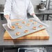 A person in a white coat holding a Chicago Metallic wire in rim aluminum sheet of cinnamon rolls.