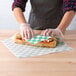 A person wearing gloves holding a sandwich with green and white Choice Deli Wrap paper.