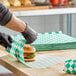 A sheet of green check deli sandwich wrap paper being used to wrap a sandwich.