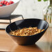 A black slanted melamine bowl filled with cereal on a table.