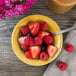 A bowl of fruit and a Tuxton Saffron monkey dish with a spoon.