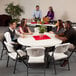 A group of people sitting around a round Lifetime folding table with white chairs.