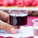 A person holding a WNA Comet clear plastic pedestal wine cup filled with red liquid.