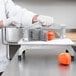 A person using a Vollrath tomato slicer to slice a tomato.