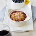 A Tuxton eggshell china casserole dish with a bowl of fruit dessert on a white plate.