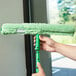 A person using an Unger Micro StripWasher with a green T-Bar to clean a window.