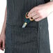 A person holding a pair of scissors in a black and white striped Chef Revival apron with a pocket.