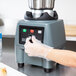 A person wearing plastic gloves using a Waring food blender.