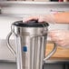 A person wearing gloves opening a stainless steel container.