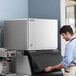 A man standing next to a large Hoshizaki water cooled ice machine.