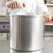 A person pouring seasoning into a large silver Vollrath stock pot.