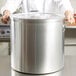 A chef holding a large silver Vollrath stock pot.