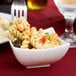 A fork in a white square porcelain bowl of pasta with sauce.